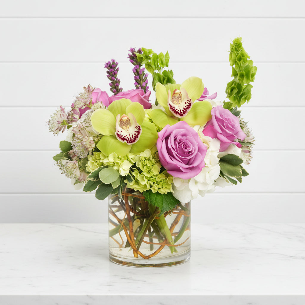 Bouquet of flowers with green orchids, pink roses, and white flowers in a clear vase on a white background