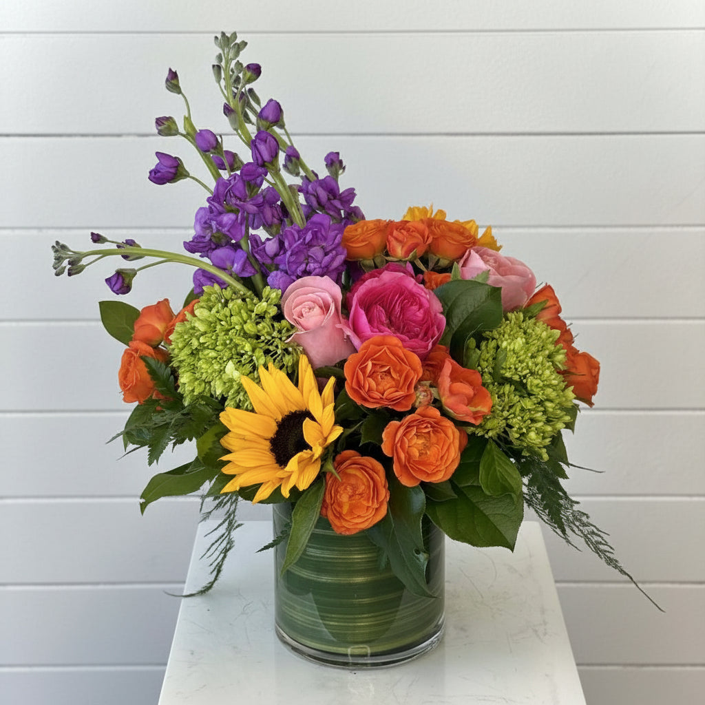 Colorful flower bouquet with a variety of flowers in a clear vase on a white surface.