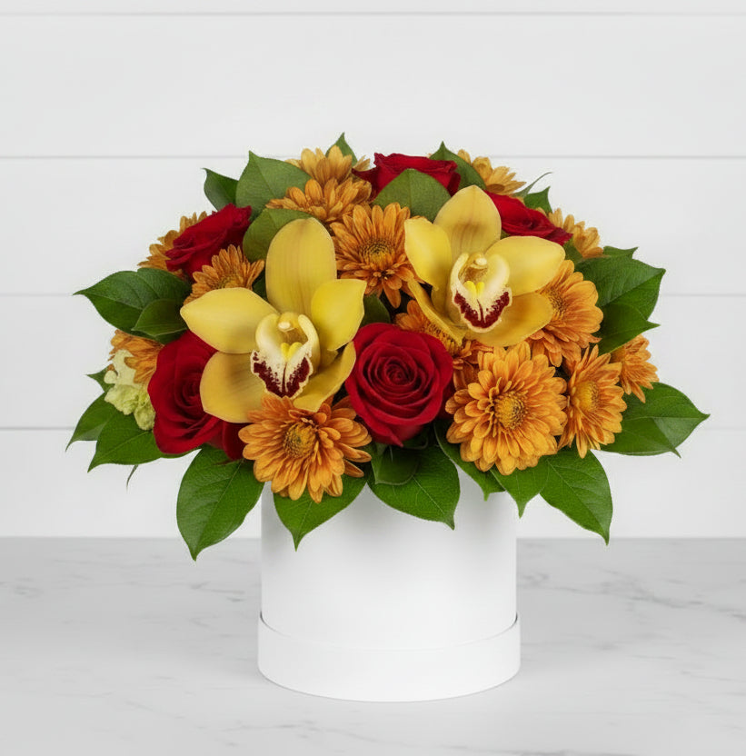 A vibrant floral arrangement featuring red roses, yellow orchids, and orange pincushion protea in a simple white cylindrical vase, set against a solid white background.