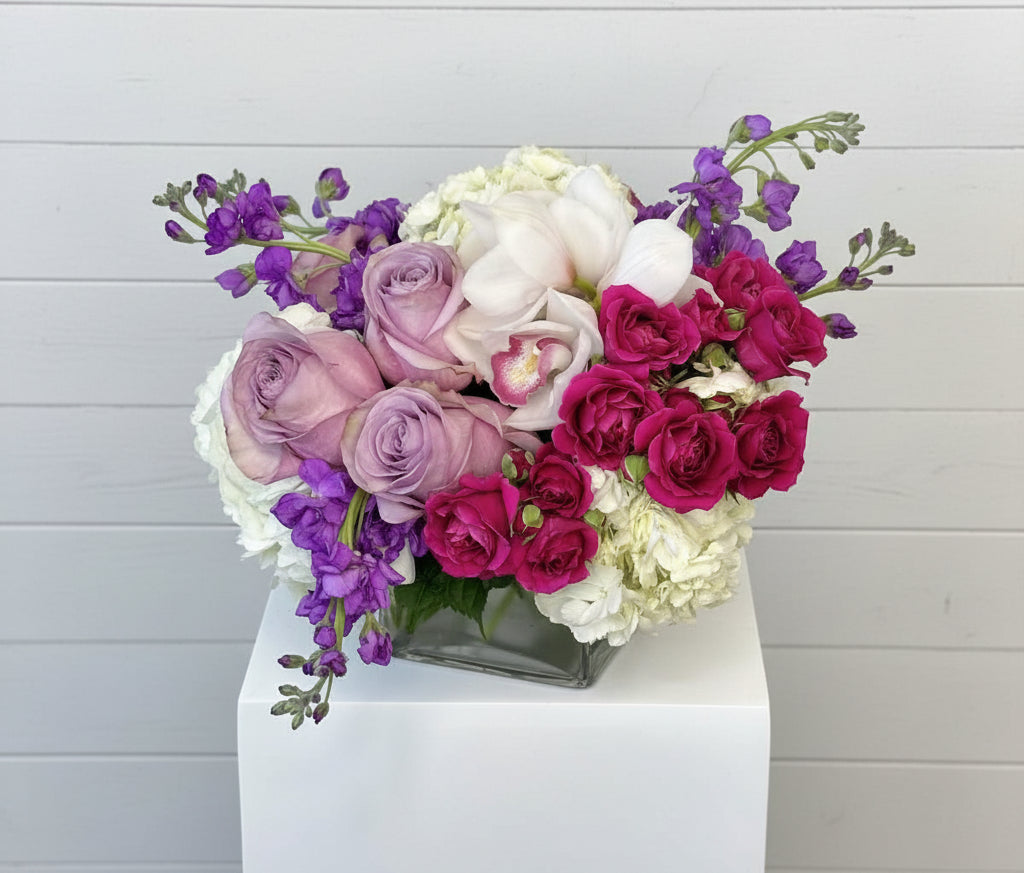 Heart-shaped arrangement of pink, purple, and white flowers on a gray background
