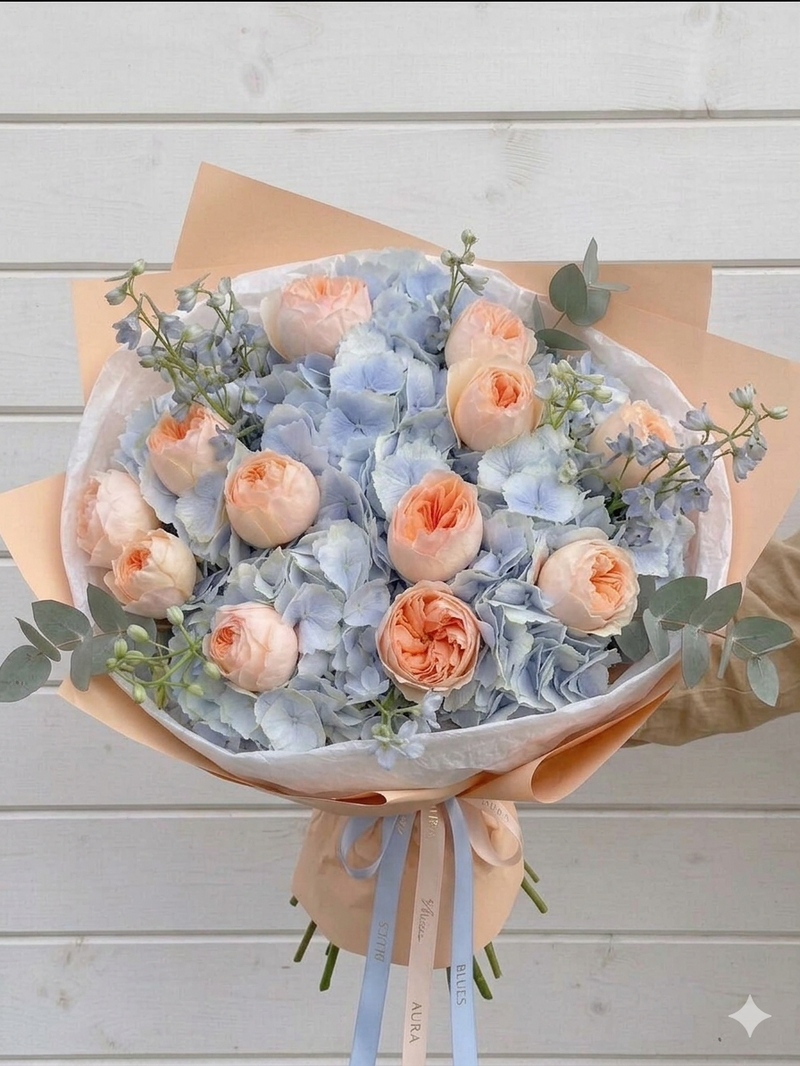 Bouquet of peach and light blue flowers with greenery on a wooden surface