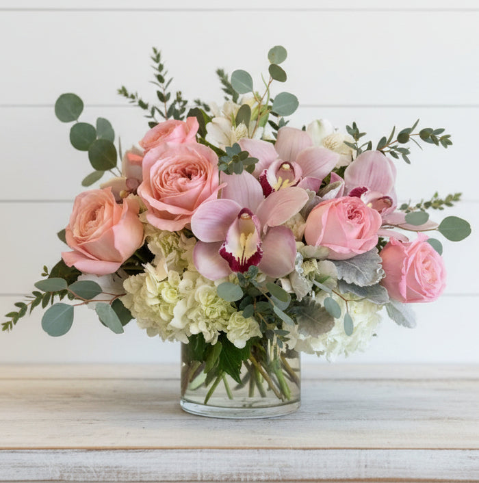 Bouquet of pink roses and orchids in a clear vase on a wooden surface with a white background