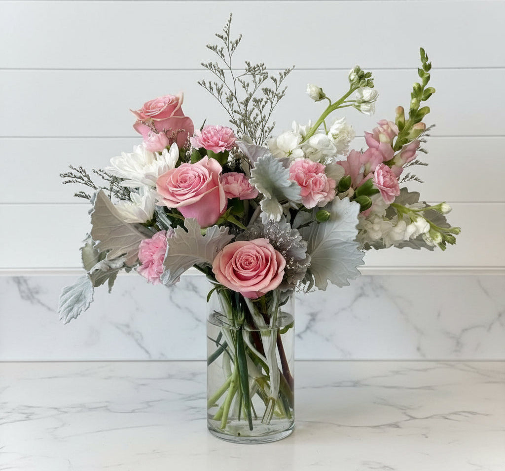 Bouquet of pink and white flowers in a clear vase on a white surface with a light gray background