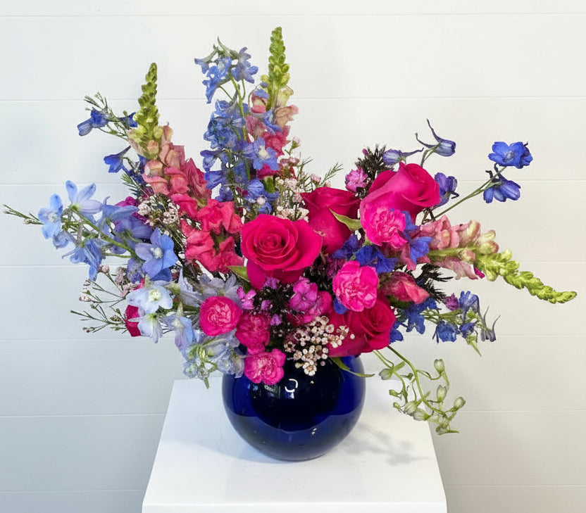 Colorful flower arrangement in a blue vase on a white surface with a light gray background