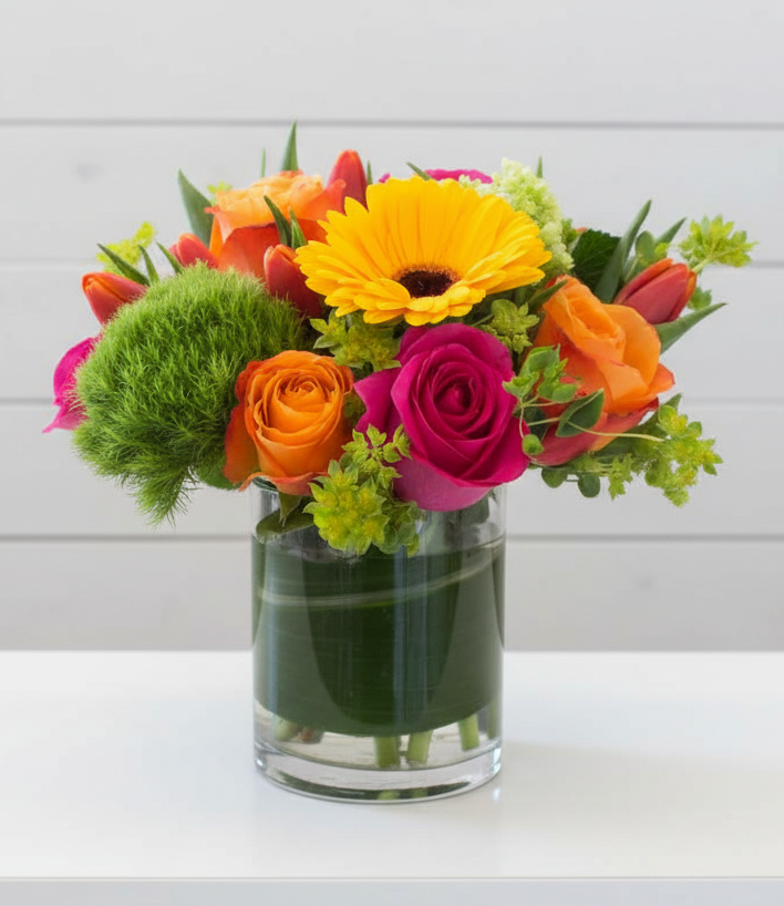 Colorful flower arrangement in a clear vase on a white surface with a light gray background